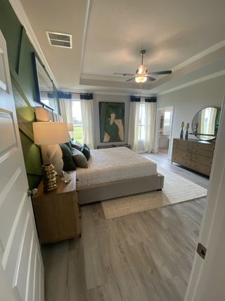 Model Home A serene bedroom featuring a modern ceiling fan, stylish artwork, and sleek wood flooring.