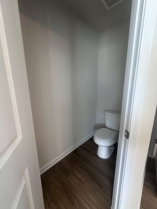 A compact bathroom with wood-style flooring and neutral walls, featuring a sleek white toilet for a minimalist design.