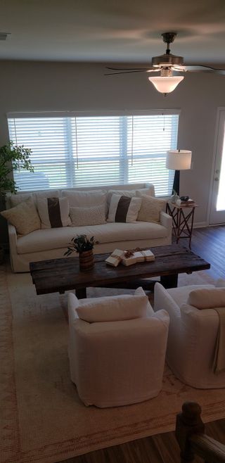 A cozy living room featuring a white sofa, plush chairs, wooden coffee table, and soft lighting with large windows.
