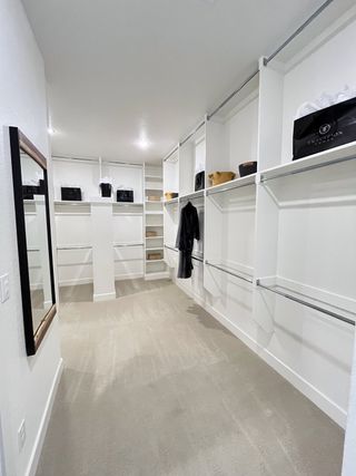 A spacious walk-in closet with ample shelving, hanging space, and soft carpeting, illuminated by modern lighting.