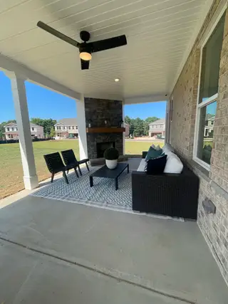 A cozy covered patio with stylish seating, a modern ceiling fan, and a stone fireplace, perfect for outdoor relaxation.