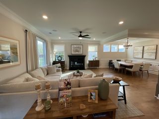 A cozy living and dining area with a plush sofa, fireplace, and elegant chandelier, featuring neutral tones and wooden accents.