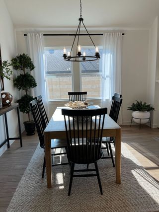 A dining room with a wooden table, black chairs, modern chandelier, and large window for natural lighting.