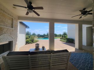 Model Home A serene patio overlooking a lush backyard with a sparkling pool and ceiling fans for breezy relaxation.