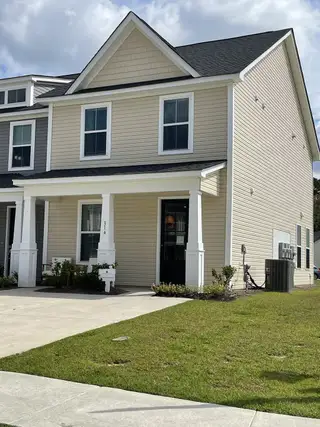 Street view A charming beige townhouse with a cozy porch in Hampton Woods by Dream Finders Homes (Summerville, SC).