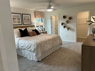 A cozy bedroom featuring a plush bed, modern art, and soft carpeting, with stylish wall decor and a ceiling fan.