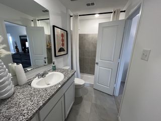 A sleek bathroom with granite countertops, open shelving, and a tiled bathtub-shower combo.