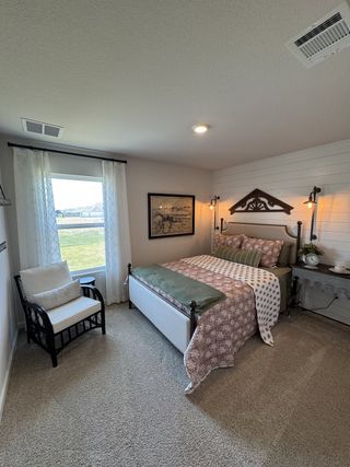A cozy bedroom featuring a patterned bedspread, rustic wall decor, and a comfortable chair near a bright window.