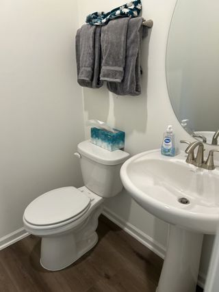 A compact bathroom with a pedestal sink, oval mirror, and soft towels, accented by wood-look flooring.