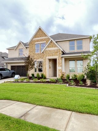 Street view A beautiful stone and brick home with lush landscaping in Stone River Glen 60s by Bloomfield Homes (Royse City, TX).