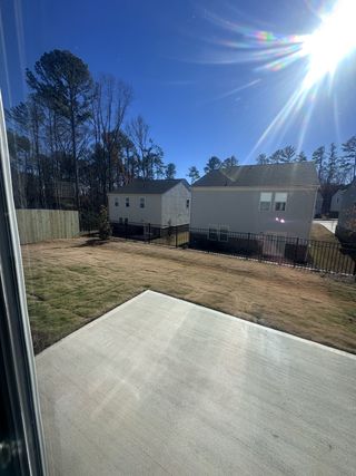 Street view A sunny backyard with a concrete patio, manicured lawn, and trees in the distance.