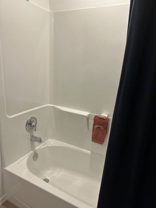 A sleek bathroom features a modern bathtub with chrome fixtures, complemented by a dark curtain and neatly folded towel.