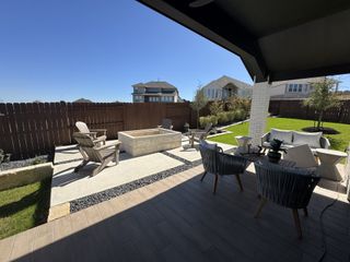 A cozy backyard patio with comfortable seating, a stone fire pit, and a lush lawn, perfect for outdoor entertaining.