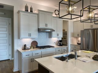 Model Home A modern kitchen with white cabinetry, sleek countertops, and geometric lighting for a stylish cooking space.
