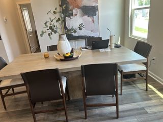 Model Home A modern dining area with a light wooden table, dark chairs, abstract art, and natural light.