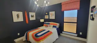Fun, superhero-themed kids’ room with a bold blue accent wall, framed artwork, and a colorful bedspread.