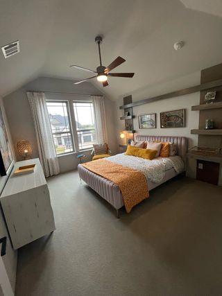 A cozy bedroom with a modern fan, built-in shelves, and neutral tones highlighted by orange accents.