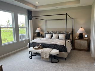 Model Home A cozy bedroom with a four-poster bed, elegant lamps, and large windows offering natural light. Neutral tones enhance relaxation.