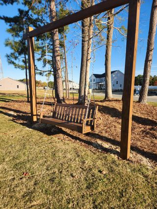 A charming wooden swing under pine trees in Grove At Gin Branch by Mattamy Homes, Wendell, NC.