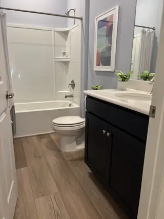 A modern bathroom with wood floors, sleek white fixtures, and minimalistic art.