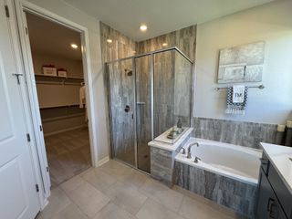 A modern bathroom with a glass shower, gray-tiled walls, and a luxurious bathtub next to a spacious walk-in closet.