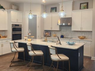Model Home A modern kitchen featuring a large island, pendant lights, and white cabinetry with stainless steel appliances.