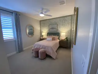 A cozy bedroom featuring floral wallpaper, soft pink bedding, a round mirror, and elegant lighting for a serene ambiance.