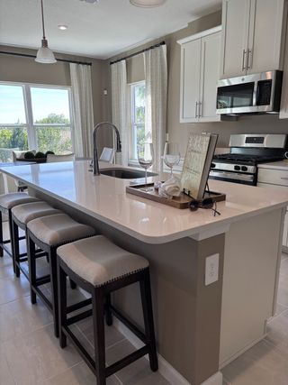 A modern kitchen with sleek white cabinetry, a central island, pendant lighting, and stainless steel appliances.