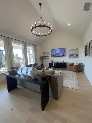 A spacious living room with vaulted ceilings, large windows, and a black chandelier in Solterra Texas by Shaddock Homes (Mesquite, TX).