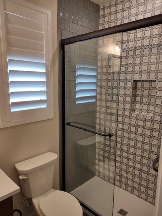 Model Home A modern bathroom featuring a geometric-tiled shower, glass door, and chic plantation shutters for a stylish touch.