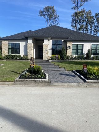 A modern home with stone accents and manicured landscaping in The Highlands 75 by Drees Custom Homes (Porter, TX).