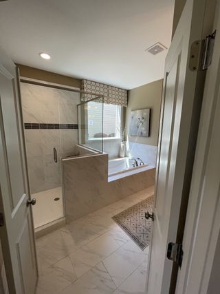 A modern bathroom featuring a sleek shower, marble-tiled bath, and elegant decor with soft lighting.