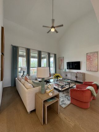 A bright living room with vaulted ceilings, a plush white sofa, vibrant coral armchairs, and hardwood floors creates a welcoming atmosphere.
