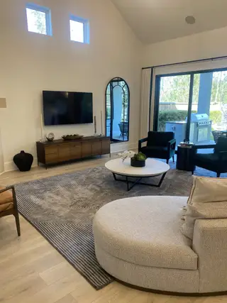 A modern living room with high ceilings, sliding glass door, and cozy seating area featuring a sleek TV unit.