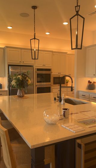 A spacious kitchen with a massive island, white cabinetry, and modern pendant lighting.