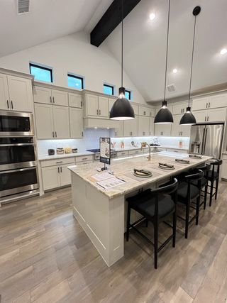 A modern kitchen with high ceilings, sleek cabinetry, a large island, pendant lighting, and stainless steel appliances.