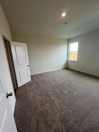 A spacious carpeted room with a single window allowing natural light, showcasing neutral walls and a simple door.
