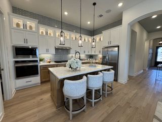 A modern kitchen featuring white cabinets, a large island with seating, pendant lighting, and sleek appliances.