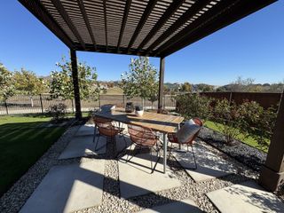 A charming outdoor patio with stylish furniture under a wooden pergola, surrounded by lush landscaping and open views.