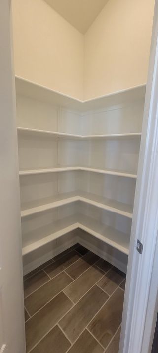 Model Home A spacious walk-in pantry with sleek white shelving and elegant tile flooring.