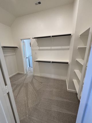 Model Home A spacious, carpeted walk-in closet with built-in shelving and ample hanging space, leading to a stylish bathroom.
