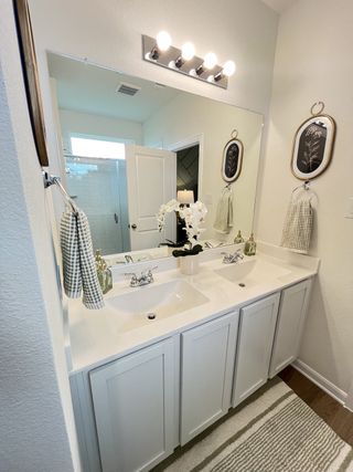 A bright bathroom with a dual-sink vanity, decorative lighting, and elegant wall art.