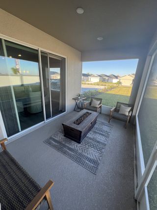 A cozy screened patio with wicker chairs, a chic fire pit, and patterned rug overlooking a serene neighborhood view.