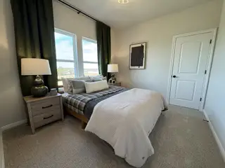 A cozy bedroom with plaid bedding, soft lighting, green curtains, and stylish artwork on the wall.