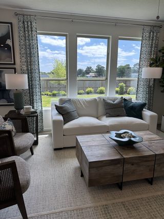 A cozy living room with a white sofa, rustic wooden table, and large windows offering a serene view.