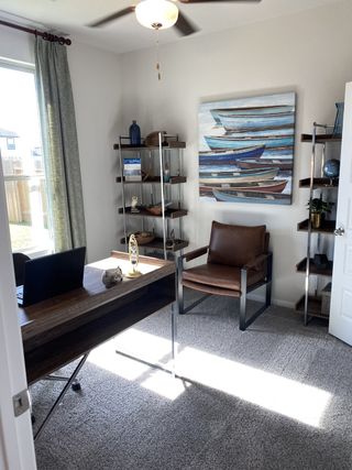 A cozy office space with a modern desk, leather chair, stylish shelves, and a nautical-themed painting.