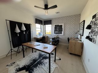 A modern office space with patterned wallpaper, a cowhide rug, and ample natural light, featuring a desk setup and photography equipment.