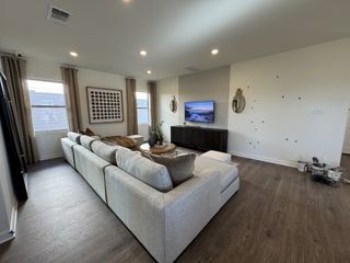 A spacious and inviting living room with a large sectional sofa in a soft gray tone. A flat-screen TV is mounted on the wall, and a dark wood entertainment center sits below.