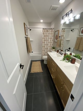 A modern bathroom featuring dark tiles, a dual sink vanity, chic lighting, and decorative elements for a cozy ambiance.
