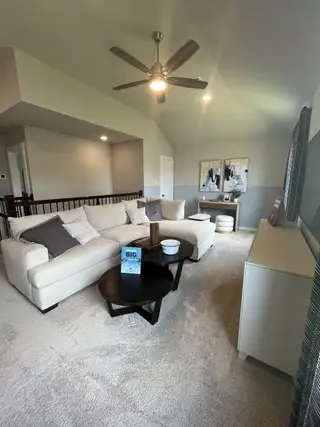 A cozy living room with a plush sectional sofa, modern ceiling fan, and abstract art creating a serene ambiance.